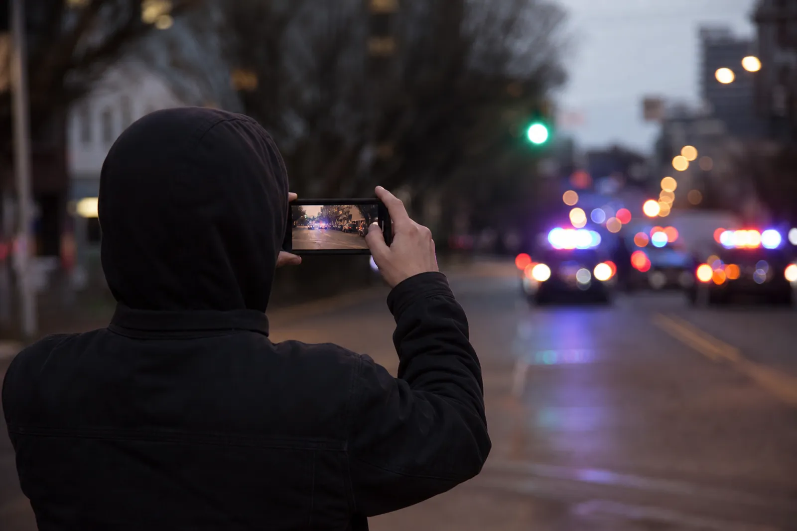 Personne filmant avec son smartphone une scène dans une rue, de loin, en gardant ses distances.