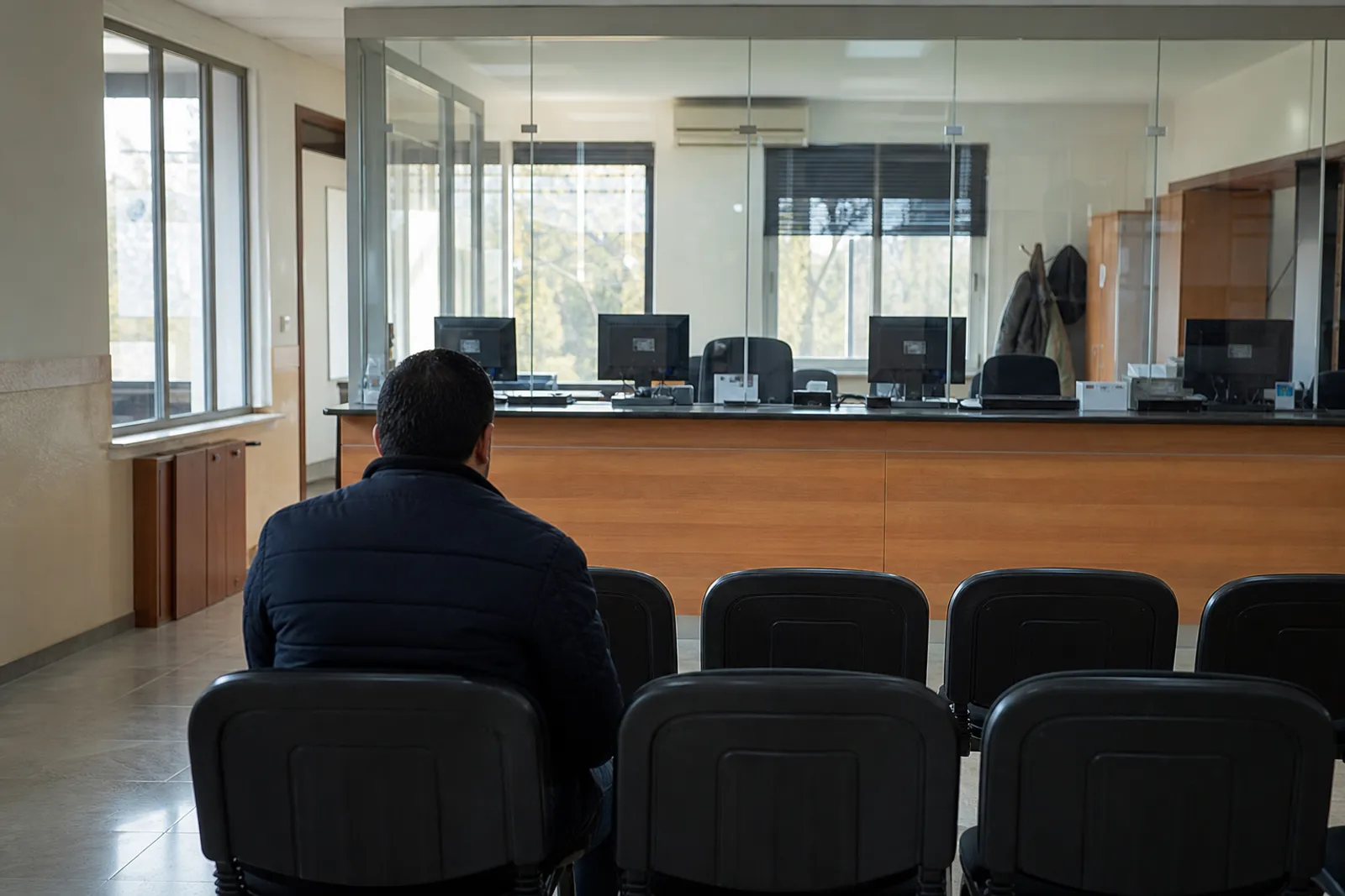 Une salle d'attente sobre de commissariat avec des chaises alignées face à un bureau administratif vitré.