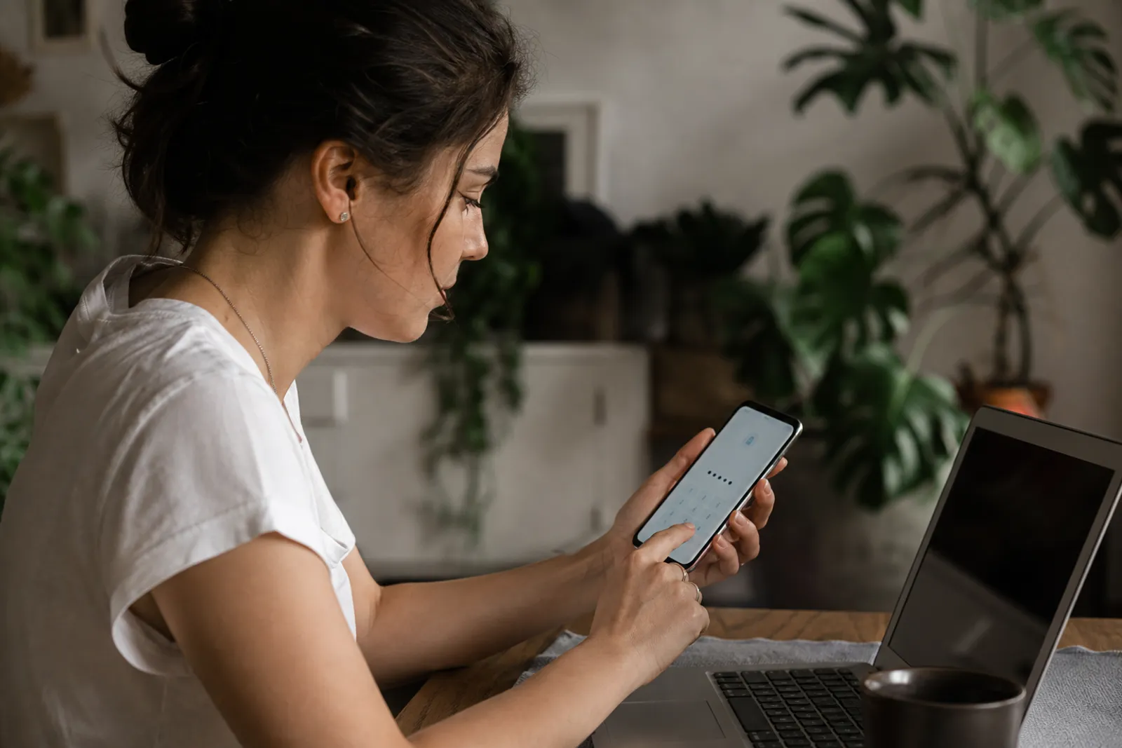 Une personne saisit un code de vérification sur son smartphone à côté d'un ordinateur portable, dans un intérieur lumineux.