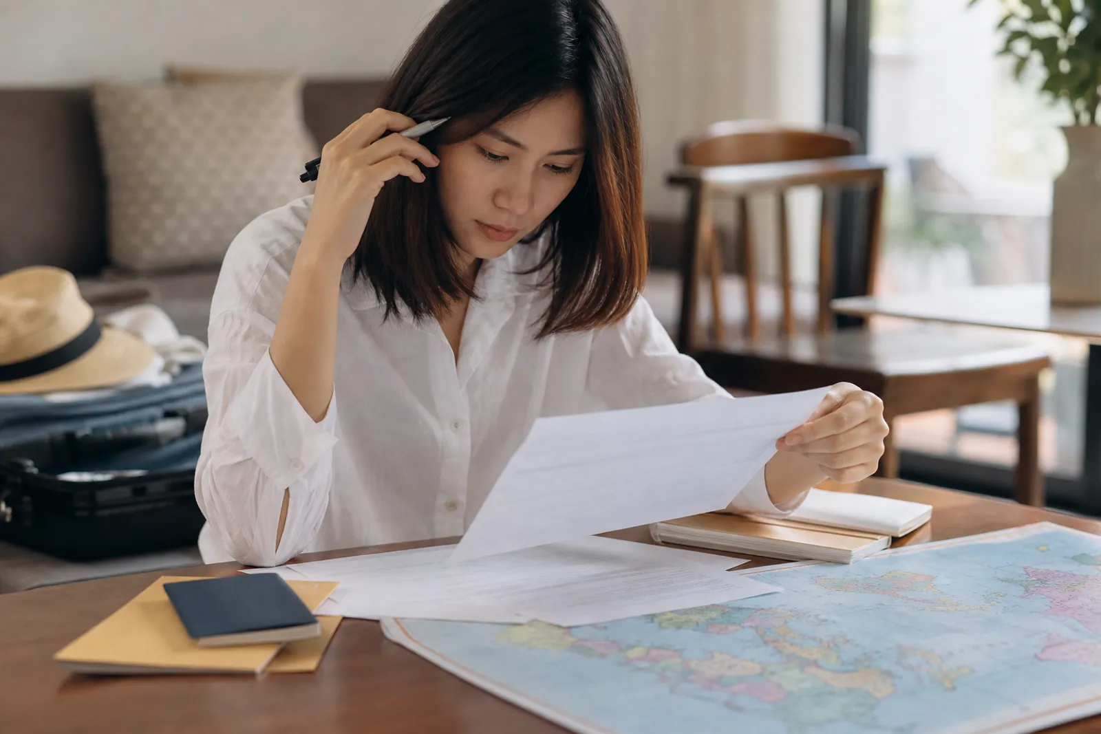 Une personne consulte des documents d'assurance voyage sur une table, avec un passeport et une carte du monde en arrière-plan.