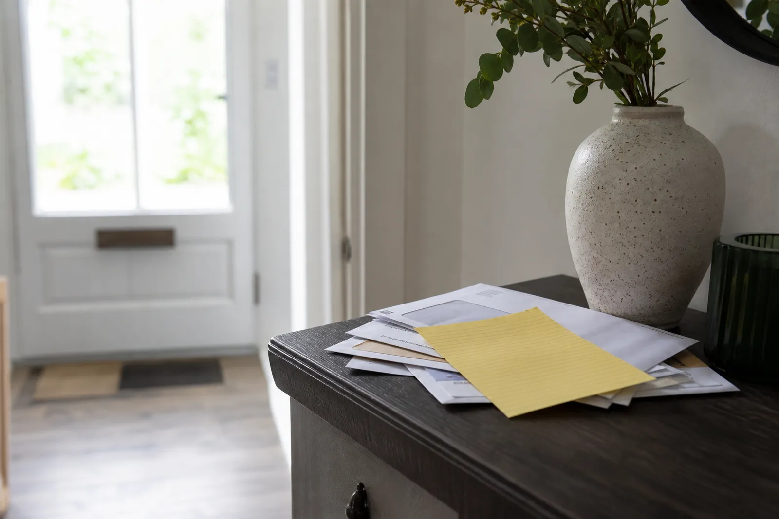 Un avis de passage postal jaune posé sur une pile de courrier dans une entrée d'appartement lumineuse.