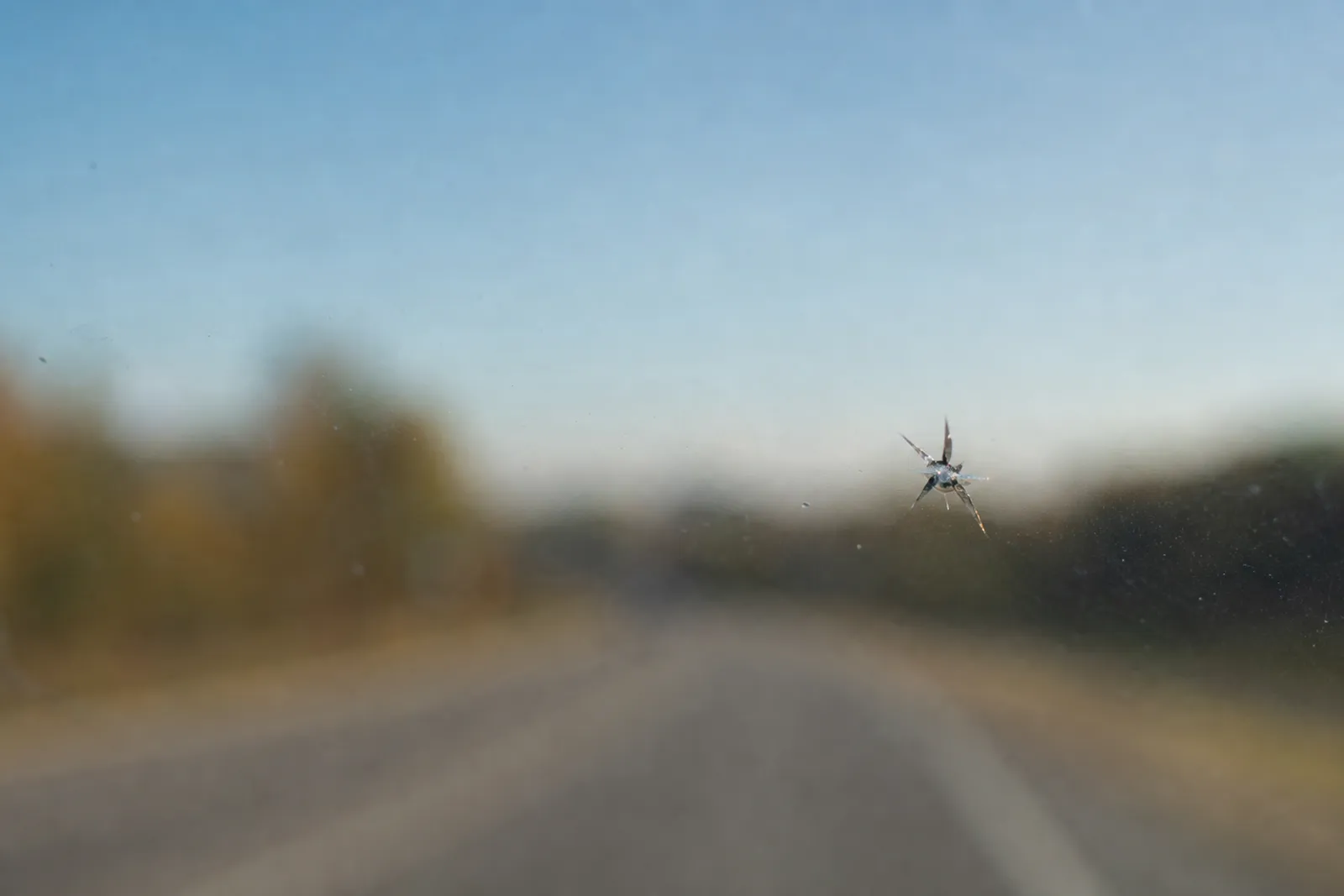 Gros plan sur un pare-brise de voiture présentant un impact en étoile, avec la route floue en arrière-plan.