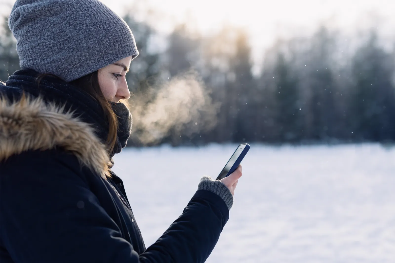 Une main tenant un smartphone dehors en hiver, avec de la buée et un pourcentage de batterie visible à l'écran.